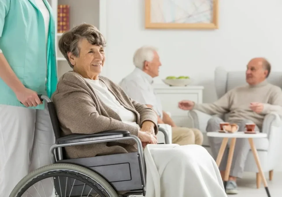 A woman in a wheelchair with two other people sitting on the couch.